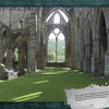Sunlight streams through tall, arched windows of a stone abbey ruin, casting shadows on grassy floors—evoking scenes from Haunted Britain by Schiffer Publishing, Ltd., with green hills and trees visible under a clear sky.