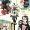 A woman with glasses stands in an art-filled room wearing a black cat shirt. She holds "Mommy's New Tattoo" by Schiffer Publishing, Ltd., surrounded by bold decor: panther tattoo art, a moon and stars portrait, skull sculpture, and lucky cat figure.