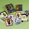 A set of colorful oracle cards by Mindy Lighthipe, called Nature's Wisdom Oracle, featuring animal, insect, and plant illustrations, is spread out on a green surface with the deck's box also visible among the cards.