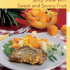 A plate with cooked steak and herbs beside colorful fruit, with a bowl of assorted fruit and pineapple in the background, inspired by "Cooking with Mustard" from Schiffer Publishing, Ltd.