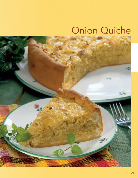 A slice of onion quiche sits on a decorated plate with herbs, next to a larger quiche, fork, and colorful napkin. Explore how various mustards enhance this dish in "Cooking with Mustard" by Schiffer Publishing, Ltd.