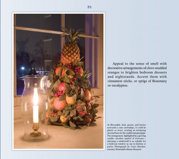 The book "Delicious Christmas Decorations at Historic Houses and Your Home" by Schiffer Publishing, Ltd. shows Colonial Williamsburg-style displays of pineapples, oranges, apples, and greenery in festive windowsills beside candlelight at dusk.
