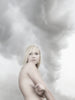 A blonde woman stands with her arms crossed, gazing ahead against swirling gray clouds—a moody, ethereal scene evocative of Iceland, featured in "Bare Landscapes" from Schiffer Publishing, Ltd.