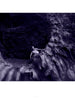 A person sits on jagged rocks at a cave entrance, surrounded by textured stone and a purple hue—an image from "Bare Landscapes" by Schiffer Publishing, Ltd., evoking the dramatic mood typical of Iceland landscape photography.