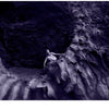 A person sits on jagged rocks at a cave entrance, surrounded by textured stone and a purple hue—an image from "Bare Landscapes" by Schiffer Publishing, Ltd., evoking the dramatic mood typical of Iceland landscape photography.