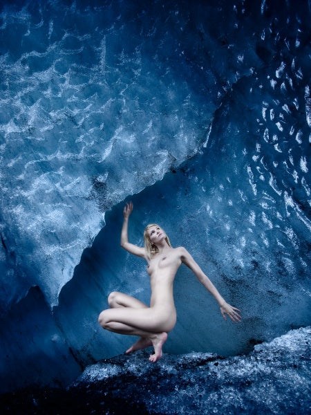 A nude figure poses elegantly in a blue-toned ice cave with textured walls and cool reflections, evoking fine Iceland photography—an image from "Bare Landscapes" by Schiffer Publishing, Ltd. that recalls sophisticated nude art books.