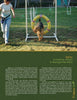 A woman guides her dog through an agility hoop in a grassy, pet-friendly yard, demonstrating ideas from "Petscaping" by Schiffer Publishing, Ltd.—a resource for creating engaging outdoor environments for pets.