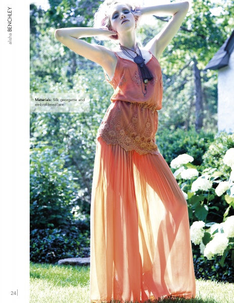 A woman in a peach dress poses outdoors amid greenery and white flowers, her arm raised. She wears sunglasses and a necklace, modeling styles from "Emerging Fashion Designers 3" by Schiffer Publishing, Ltd.