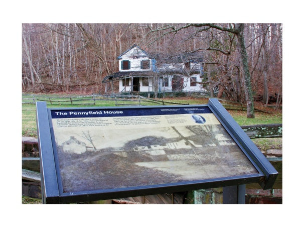 An informational sign about The Chesapeake and Ohio Canal by Schiffer Publishing, Ltd. stands in the foreground, while the old Pennyfield House appears among leafless trees in the historic canal's background.