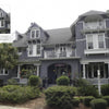 A large gray shingle-style house with white trim, featured in "Florida's Historic Victorian Homes" by Schiffer Publishing, Ltd., showcases multiple gables, balconies, palm trees, a covered front porch, and detailed upper shingles.