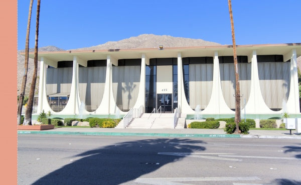 Palm Springs by Schiffer Publishing, Ltd. features a mid-century modern building with tall windows and vertical columns, evoking classic Palm Springs postcards, with mountain and palm tree views and stairs to the main entrance.