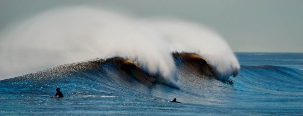 Two surfers watch a powerful Atlantic wave crest under a clear sky, embodying the thrill of surf culture as featured in "Surf NYC" by Schiffer Publishing, Ltd.