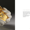 A white ceramic art bowl with flame-like edges and a gold interior sits on a gray surface. To the right, a page from "Vessels" by Schiffer Publishing, Ltd. features the poem "I Will Gather Them" in elegant, minimal text.