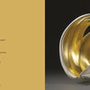 A book spread from "Vessels" by Schiffer Publishing, Ltd.: left page shows the poem "Transfiguration" on gold; right page displays Jennifer McCurdy’s white and gold, wing-like porcelain sculpture against a dark background.