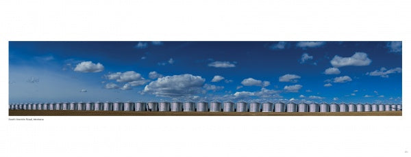 A long row of large silver grain silos stretches across flat land under a bright blue sky, evoking the sweeping vistas featured in "Yellowstone Country" by Schiffer Publishing, Ltd.