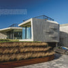 Modern Masters by Schiffer Publishing, Ltd. features a modern house with angular gray-paneled walls, large glass windows, tiered grassy landscaping, and a gray car in the driveway under a sunny blue sky, highlighting innovative architecture.
