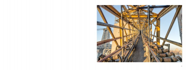 A close-up of an industrial conveyor belt framed by metal and rollers, set against the sky and structures—capturing Brooklyn's Sweet Ruin by Schiffer Publishing, Ltd., reflecting the Domino Sugar Refinery's rich industrial history.