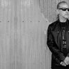 A man in sunglasses and a black leather jacket stands before a corrugated metal wall. The left side displays info about 80s Redux by Schiffer Publishing, Ltd., spotlighting 1980s musicians and music portraiture.