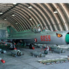 The MiG-21 by Schiffer Publishing, Ltd. features a silver and green supersonic jet numbered 8859 with a painted nose eye, displayed in an arched hangar amid bombs, missiles, and ammunition.