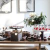 A sunlit table features assorted desserts with greenery and holiday decor, reflecting creative, modern homemaking inspiration from "Modern HomeMaker" by Schiffer Publishing, Ltd.