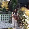 A woman in a floral dress stands in a garden holding dried hydrangeas—a scene from "Modern HomeMaker" by Schiffer Publishing, Ltd., perfect for creative homeowners seeking home décor inspiration.