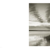 A serene black-and-white photo titled "Martha's Vineyard" by Schiffer Publishing, Ltd. shows a calm lake at sunset with tall grasses, sandy shore, and streaked clouds. Blank white space on the left evokes classic seascape photography.