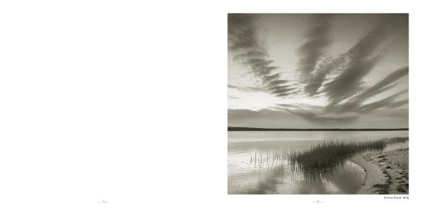 A serene black-and-white photo titled "Martha's Vineyard" by Schiffer Publishing, Ltd. shows a calm lake at sunset with tall grasses, sandy shore, and streaked clouds. Blank white space on the left evokes classic seascape photography.