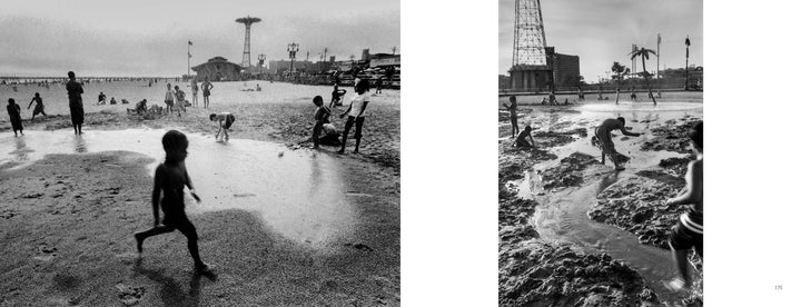 Children play in wet sand and shallow water on a lively Coney Island beach with people, buildings, and an amusement park tower in the background—captured in striking black-and-white photos from "Coney Island People" by Schiffer Publishing, Ltd.