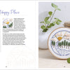 An embroidery book, Sunny Stitches by Schiffer Publishing, Ltd., lies open—left page with instructions, right with a finished landscape hoop beside a basket and plant—ideal inspiration for embroidery projects.