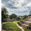 Panoramic view of ancient Mayan ruins at Palenque, featured in "Monumental" by Schiffer Publishing, Ltd., with stone temples amid lush trees in Chiapas, Mexico. A photo book-worthy stone carving detail appears on the left.