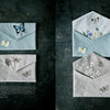 Juno's Nature Embroidery Notebook by Schiffer Publishing, Ltd. is shown on a dark surface with covers featuring delicate butterfly and flower embroidery in soft pastel and natural tones.