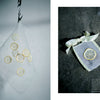 Juno's Nature Embroidery Notebook by Schiffer Publishing, Ltd. features delicate lemon slice and botanical embroidery designs, displayed on white mesh pouches—one hanging from a hook, another tied with ribbon on a dark surface.