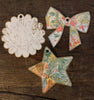 Three wooden ornaments from Schiffer Publishing’s Paint-Your-Own Holiday Decorations: a scalloped circle with an animal face, a floral-patterned bow, and a star with botanical detail, inspired by Kristy Rice’s watercolor holiday designs.