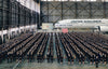 Hundreds in dark suits line up inside a hangar with a Japan Airlines plane and a screen behind—a striking image from Japan by Schiffer Publishing, Ltd., perfect for any travel photography collection.