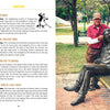An older man in a red cap poses playfully with a bronze bench statue, surrounded by plaques featuring funny facts from "Useless Knowledge for the World Traveler" by Schiffer Publishing, Ltd., amid trees and greenery.