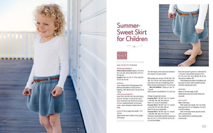 A smiling, curly-haired child models a white long-sleeve top and blue knitted skirt from "All-Year-Round Knitting for Little Sweethearts" by Schiffer Publishing, Ltd., shown on a wooden deck with highlighted KlompeLompe patterns.