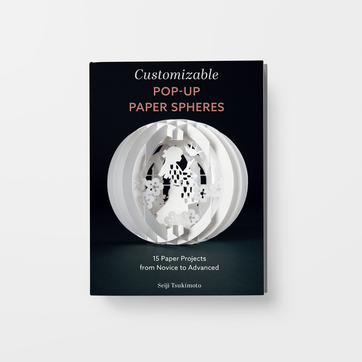 The image displays "Customizable Pop-Up Paper Spheres" by Schiffer Publishing, Ltd., featuring a 3D paper sphere design on the cover. The subtitle is "15 Customizable Paper Crafts from Novice to Advanced by Seiji Tsukimoto.