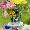 The image shows a colorful spring bouquet in a porcelain vase with matching saucer and teacup on a mosaic-tiled outdoor table, inspiring ceramic upcycles. Product: Artfully Transforming Bottles & Plates by Schiffer Publishing, Ltd. "PORCELAIN" overlays the image.