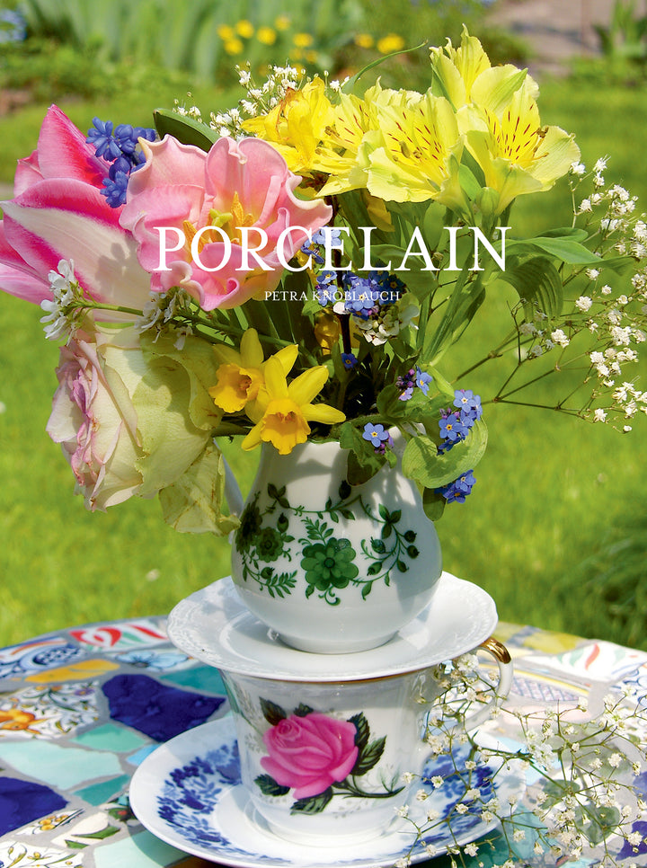The image shows a colorful spring bouquet in a porcelain vase with matching saucer and teacup on a mosaic-tiled outdoor table, inspiring ceramic upcycles. Product: Artfully Transforming Bottles & Plates by Schiffer Publishing, Ltd. "PORCELAIN" overlays the image.